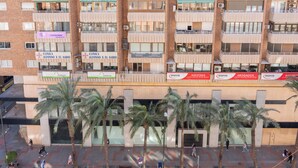 Un edificio de varios pisos con balcones, palmeras y varios letreros, incluyendo 'Clinica Alfonso X el Sabio' y 'Aurea'.