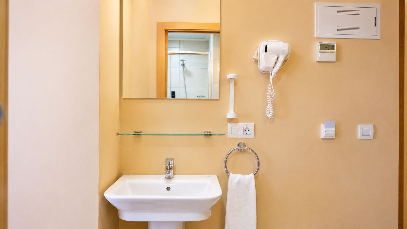 A bathroom with a sink, mirror, towel ring, hairdryer, and a wall-mounted heater.