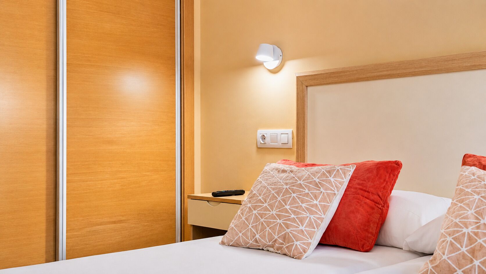 Una habitación de hotel con cama, mesita de noche y una lámpara de pared.