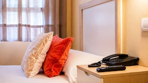 Une chambre d’hôtel avec un lit, une table de chevet avec un téléphone et des télécommandes, et une fenêtre avec des rideaux.