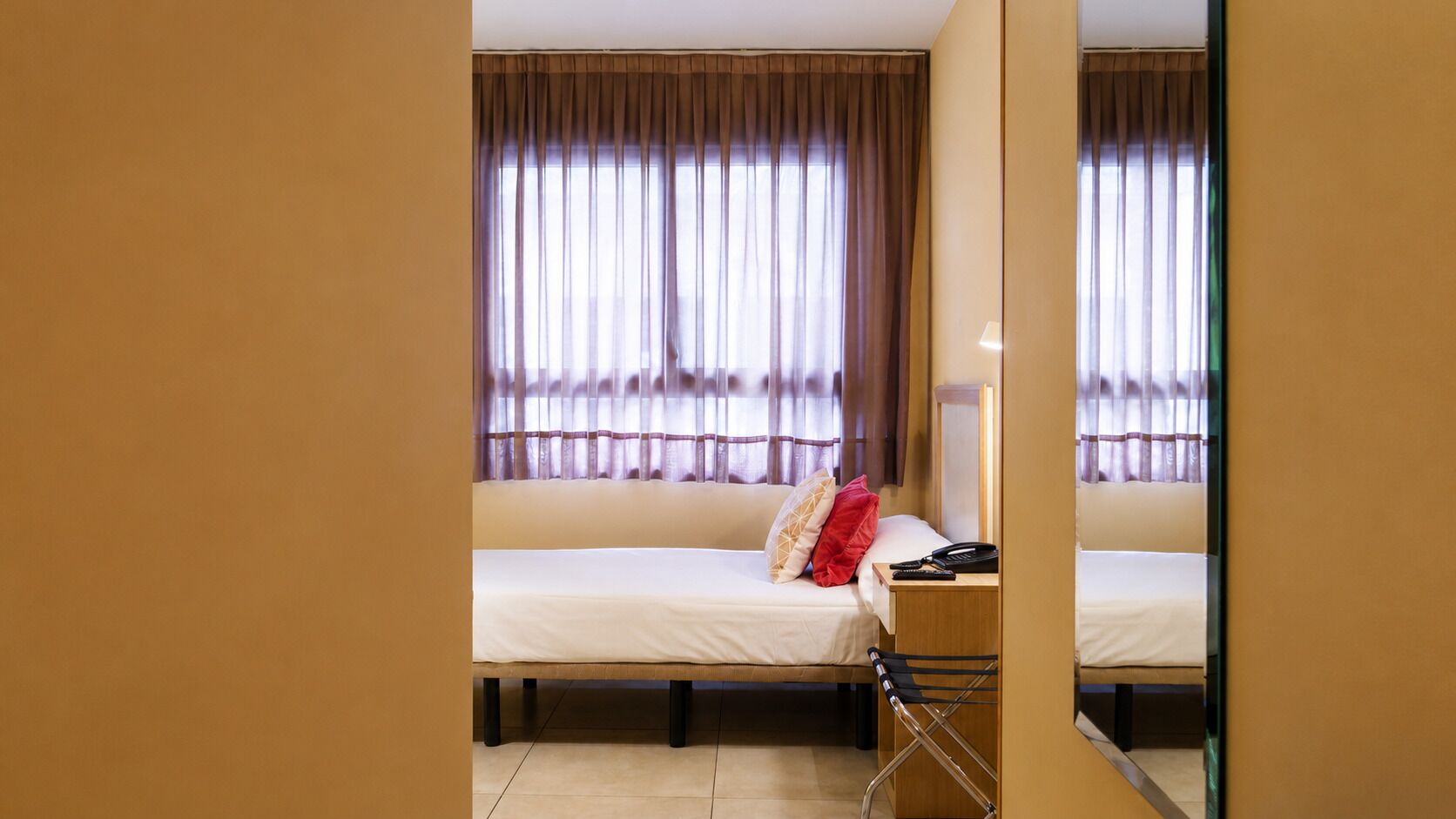 Una habitación de hotel con cama, escritorio, silla y espejo.