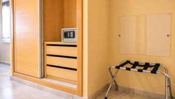 Una habitación con un armario de madera, una mesita con microondas y una silla metálica con respaldo.