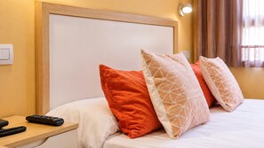 Une chambre d’hôtel comprenant un lit, des oreillers, une table de chevet, une télécommande et un luminaire fixé au mur.