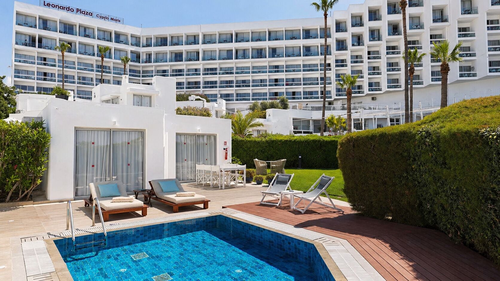A hotel with a swimming pool, lounge chairs, and a well-maintained garden.