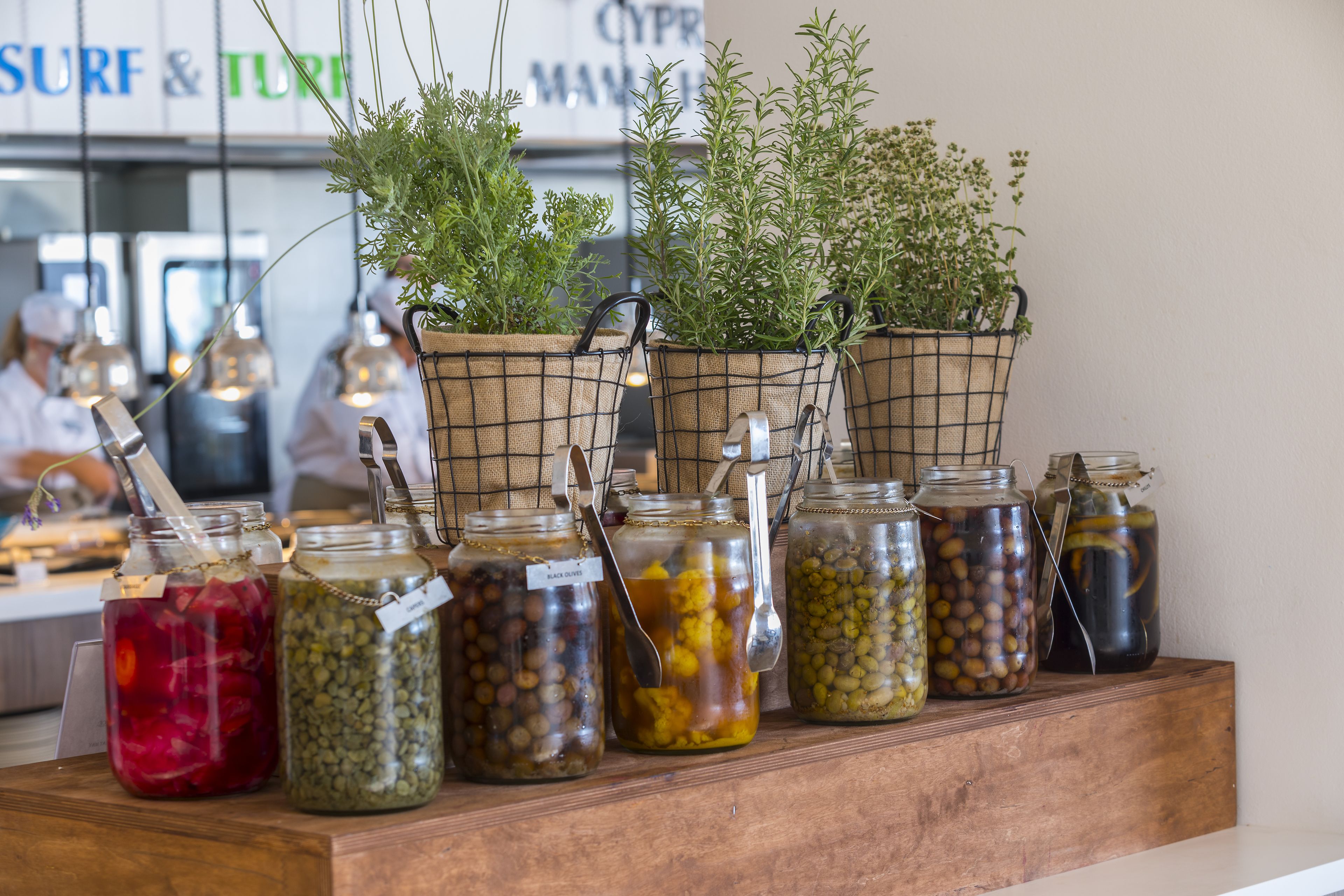 A display of jars with pickled vegetables and herbs on a wooden shelf.