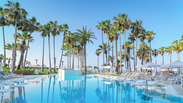 A pool area with palm trees, lounge chairs, and umbrellas. - Leonardo Plaza Cypria Maris Beach Hotel & Spa (Geroskipou)