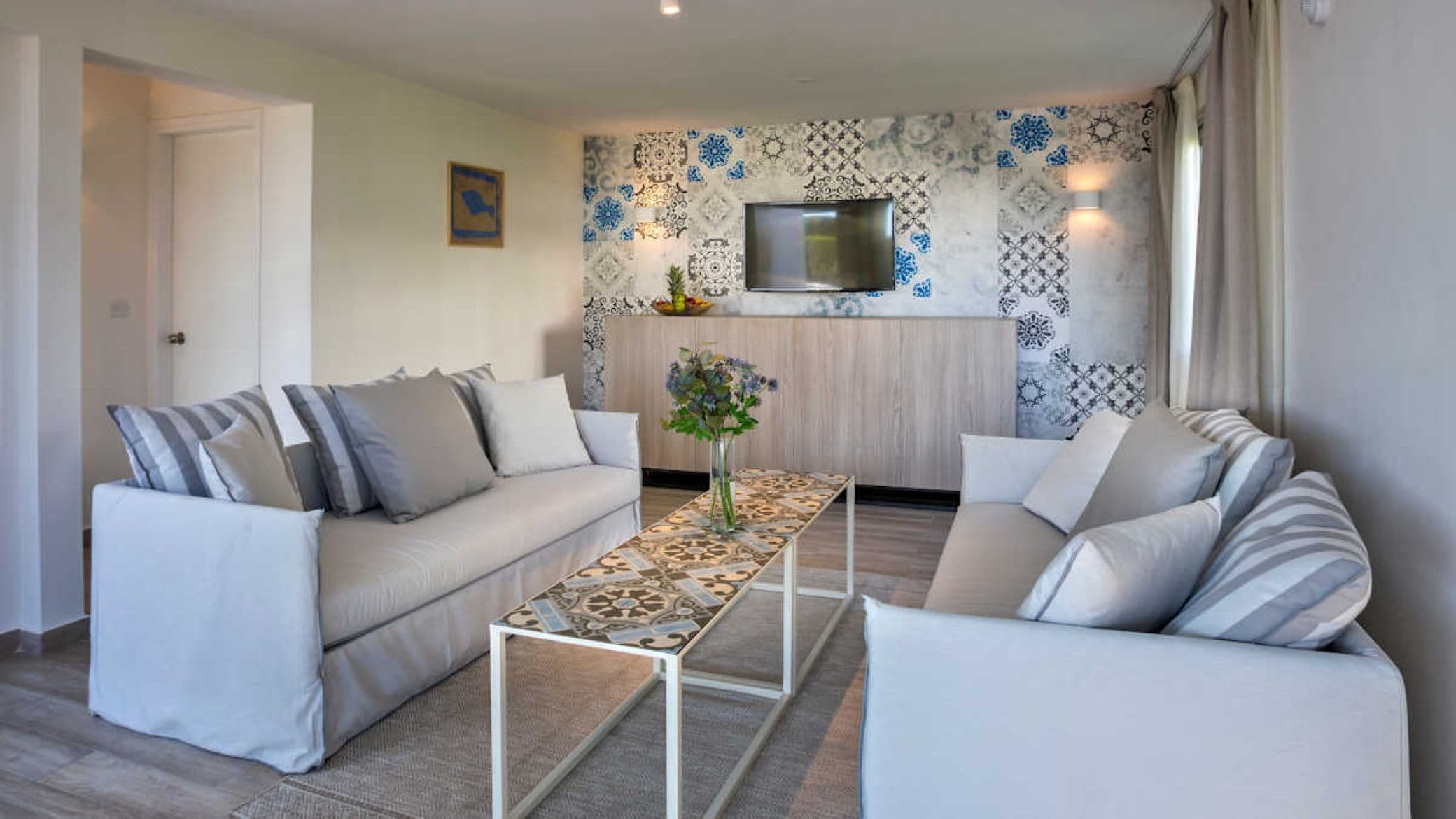 Een moderne woonkamer met twee banken, een salontafel en een aan de muur bevestigde televisie.