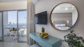 Una habitación de hotel moderna con balcón, un televisor montado en la pared, un espejo redondo y un frutero sobre una consola azul.