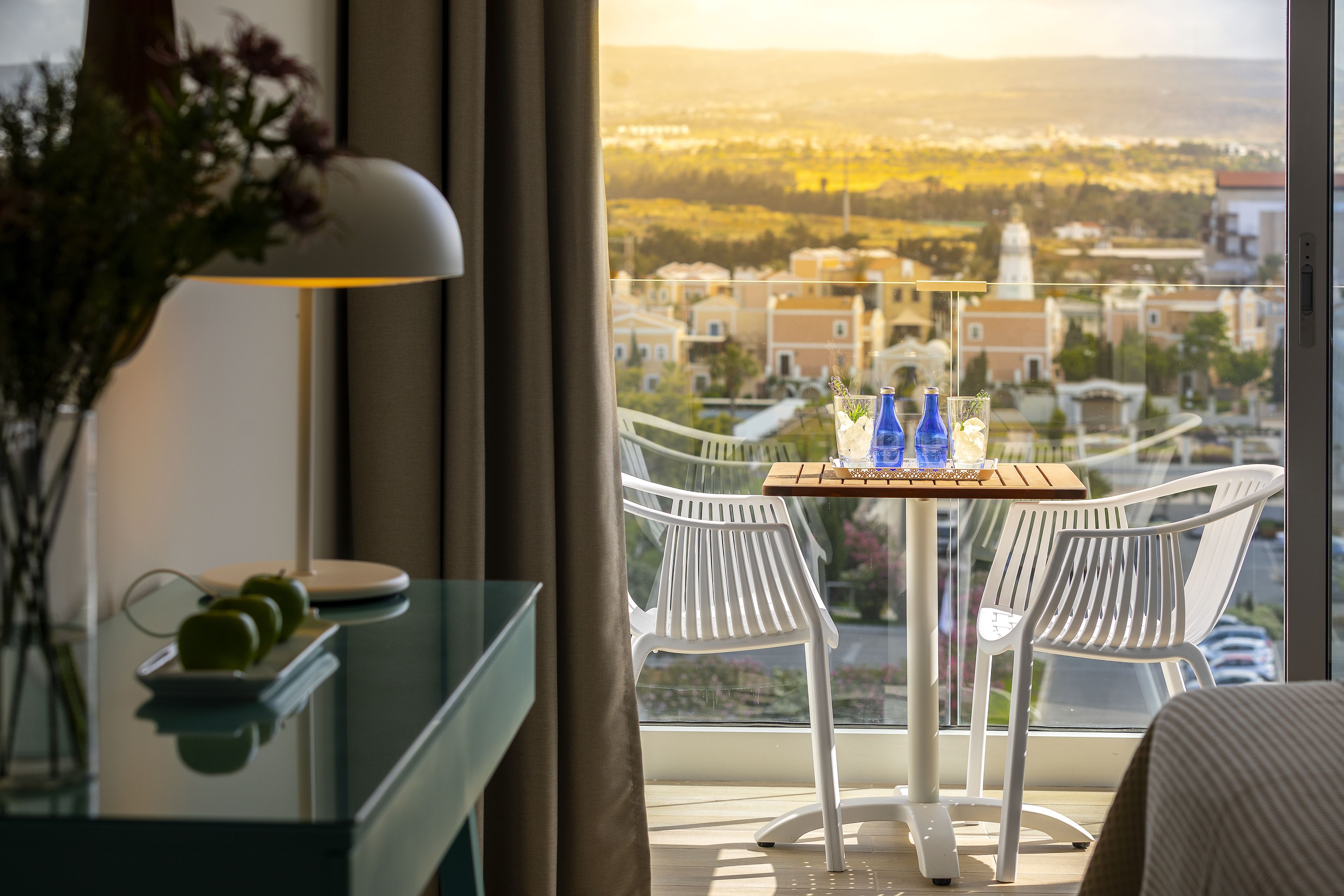 A balcony with a table, two chairs, and a view of a cityscape.