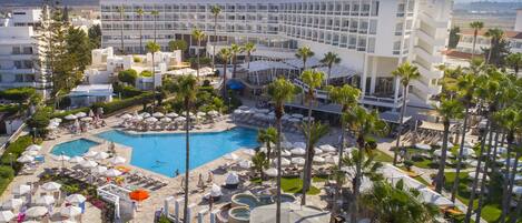 Um hotel com várias piscinas, palmeiras e espreguiçadeiras.