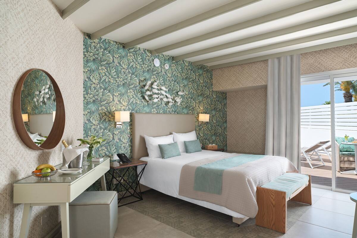 Een hotelkamer met een bed, nachtkastjes, een bureau en een balkon met tuinmeubilair.