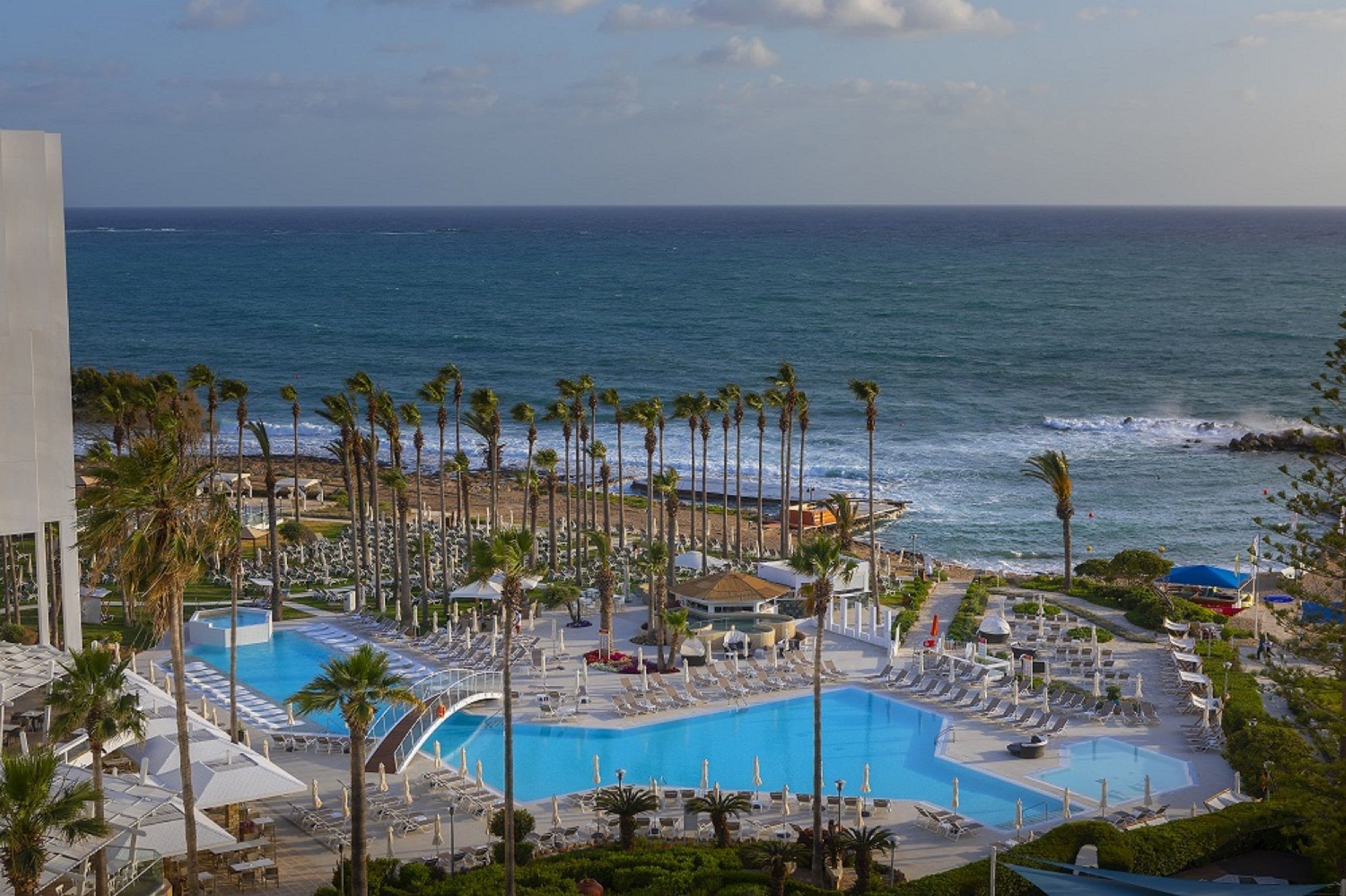 A resort with a large pool, palm trees, and a view of the ocean.