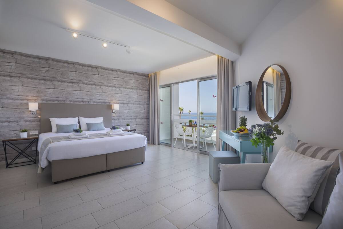 Een moderne hotelkamer met een groot bed, een bank, een eethoek en een balkon met uitzicht op zee.