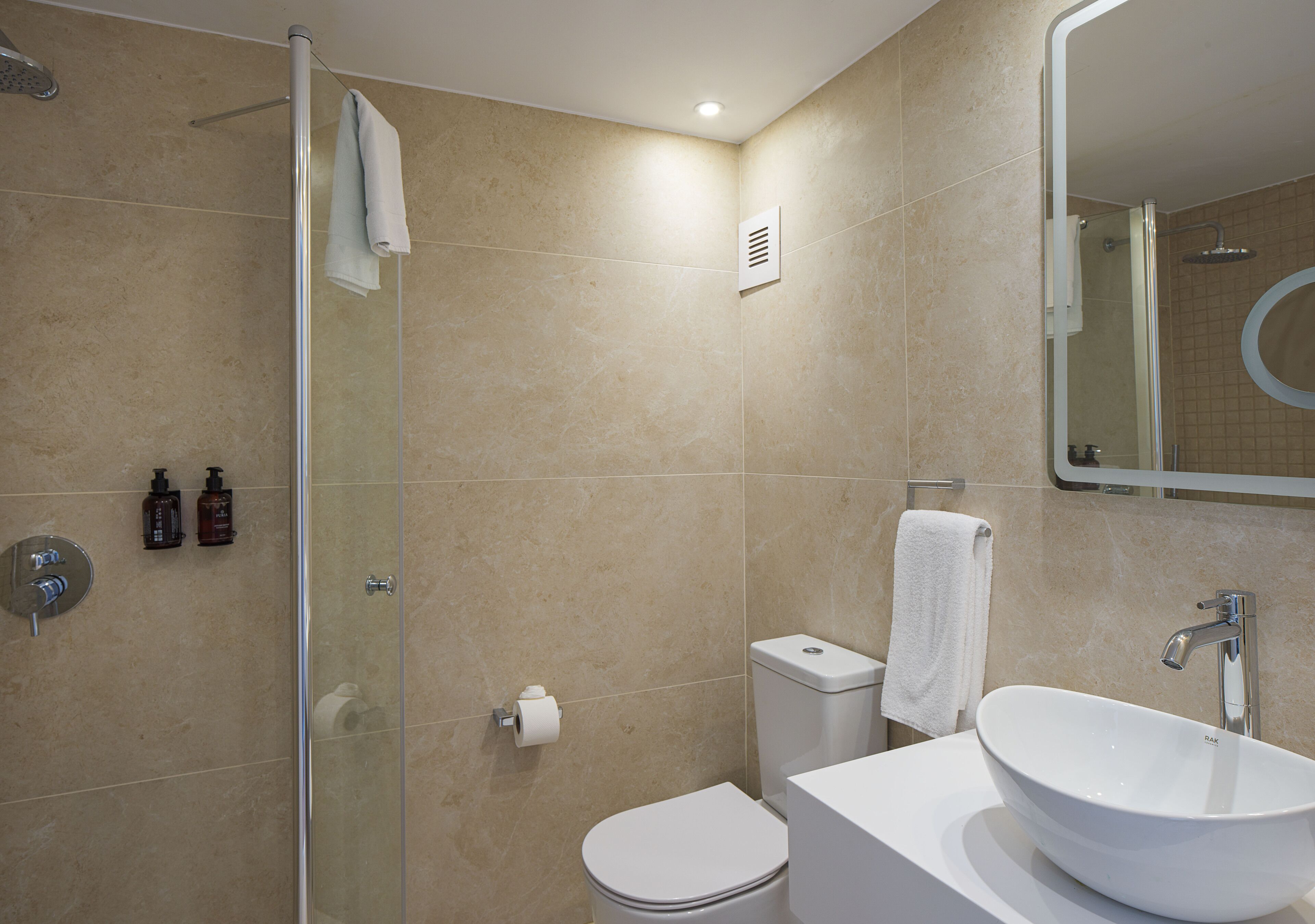 A bathroom with a glass shower enclosure, a toilet, a sink with a mirror, and a towel hanging on the wall.