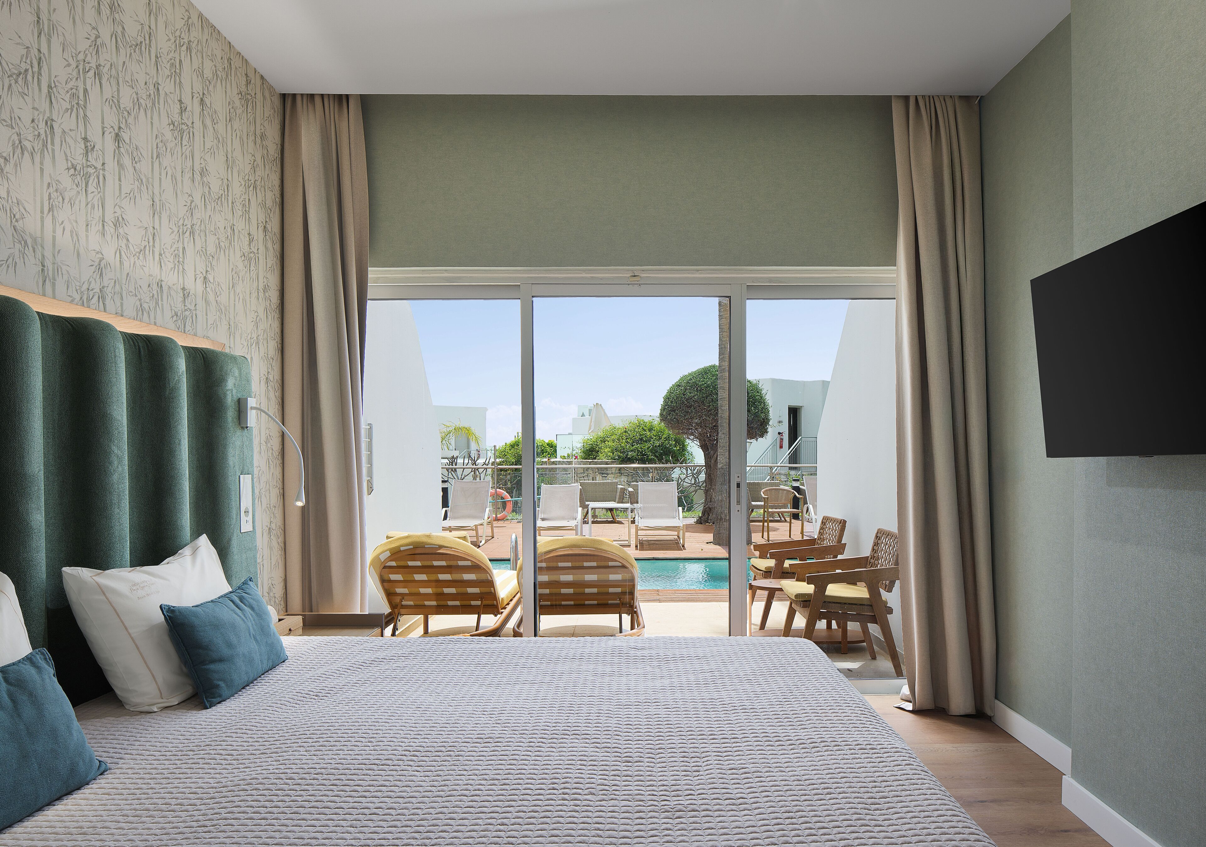 Hotelkamer met groot bed, uitzicht op het zwembad en terras, plus een wandgemonteerde flatscreen-tv.