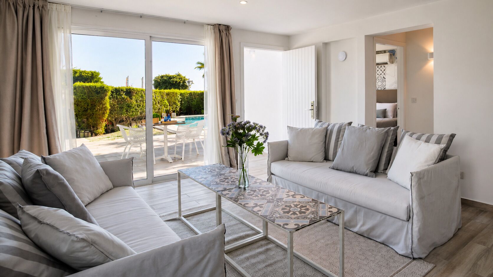 A modern living room with a sofa, a coffee table, and a view of a pool and greenery outside.