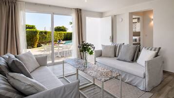 A modern living room with a sofa, a coffee table, and a view of a pool and greenery outside.