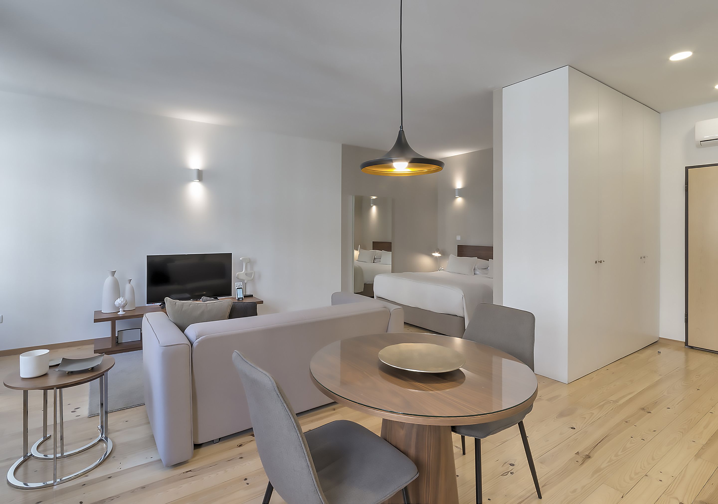 A modern hotel room with a sofa, a round dining table, a TV, and a bed.