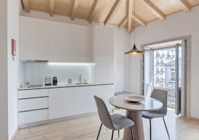 Uma cozinha moderna com armários brancos, uma mesa de jantar redonda e vista para uma varanda.