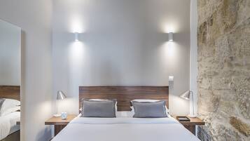 A modern hotel room with a large bed, two bedside tables with lamps, a wooden headboard, and a stone wall.