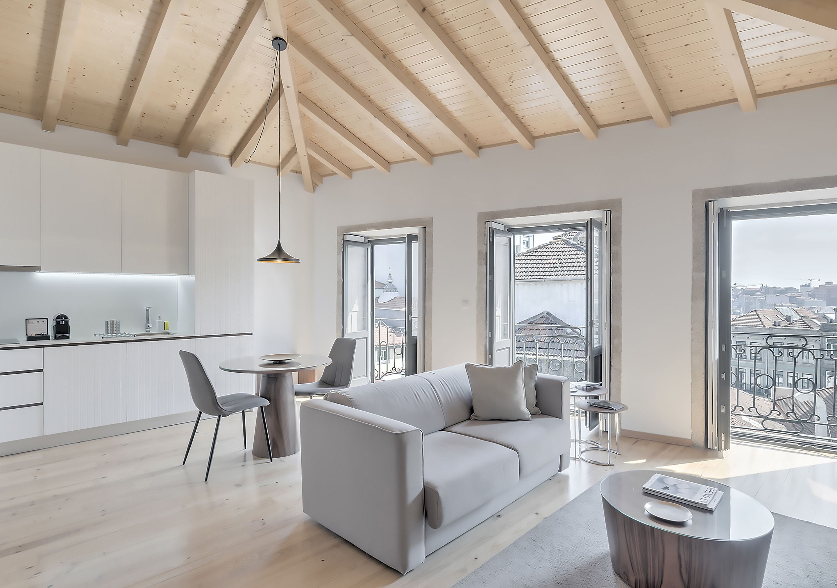 A modern living room with a grey sofa, a dining table, and a view of the city through large windows.