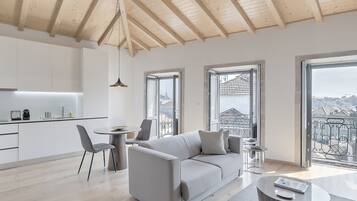 A modern living room with a grey sofa, a dining table, and a view of the city through large windows.