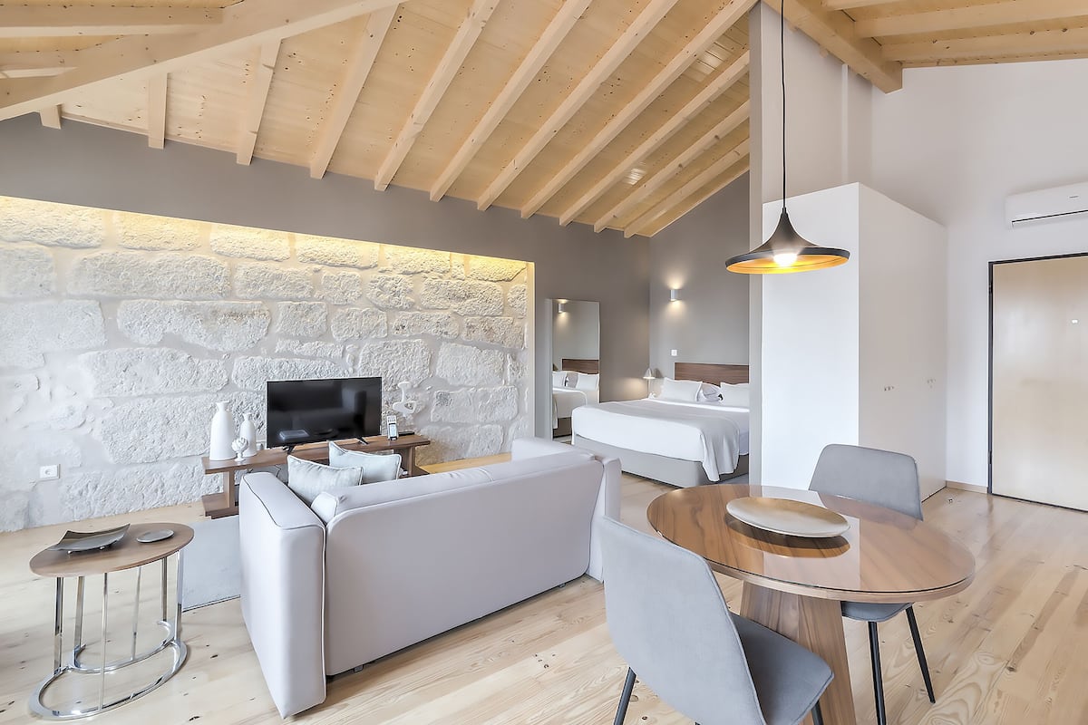 A modern living room with a stone wall, wooden ceiling beams, a sofa, a TV, and a dining area with a table and chairs.