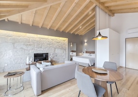 Uma sala de estar moderna com parede de pedra, vigas de madeira no teto, um sofá, uma TV e um espaço de jantar com mesa e cadeiras.