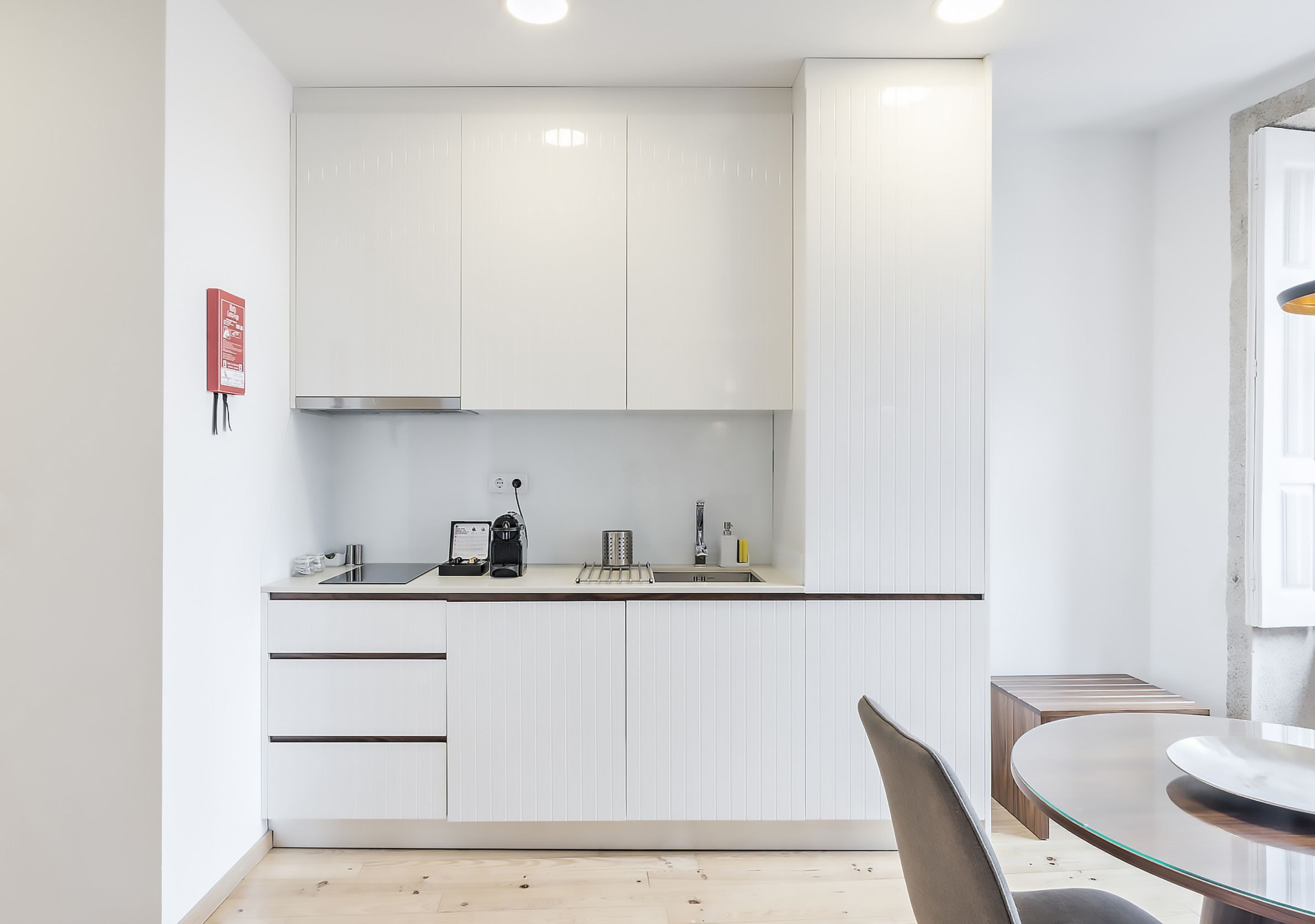 A modern kitchen with white cabinets, a stainless steel sink, and a glass dining table.