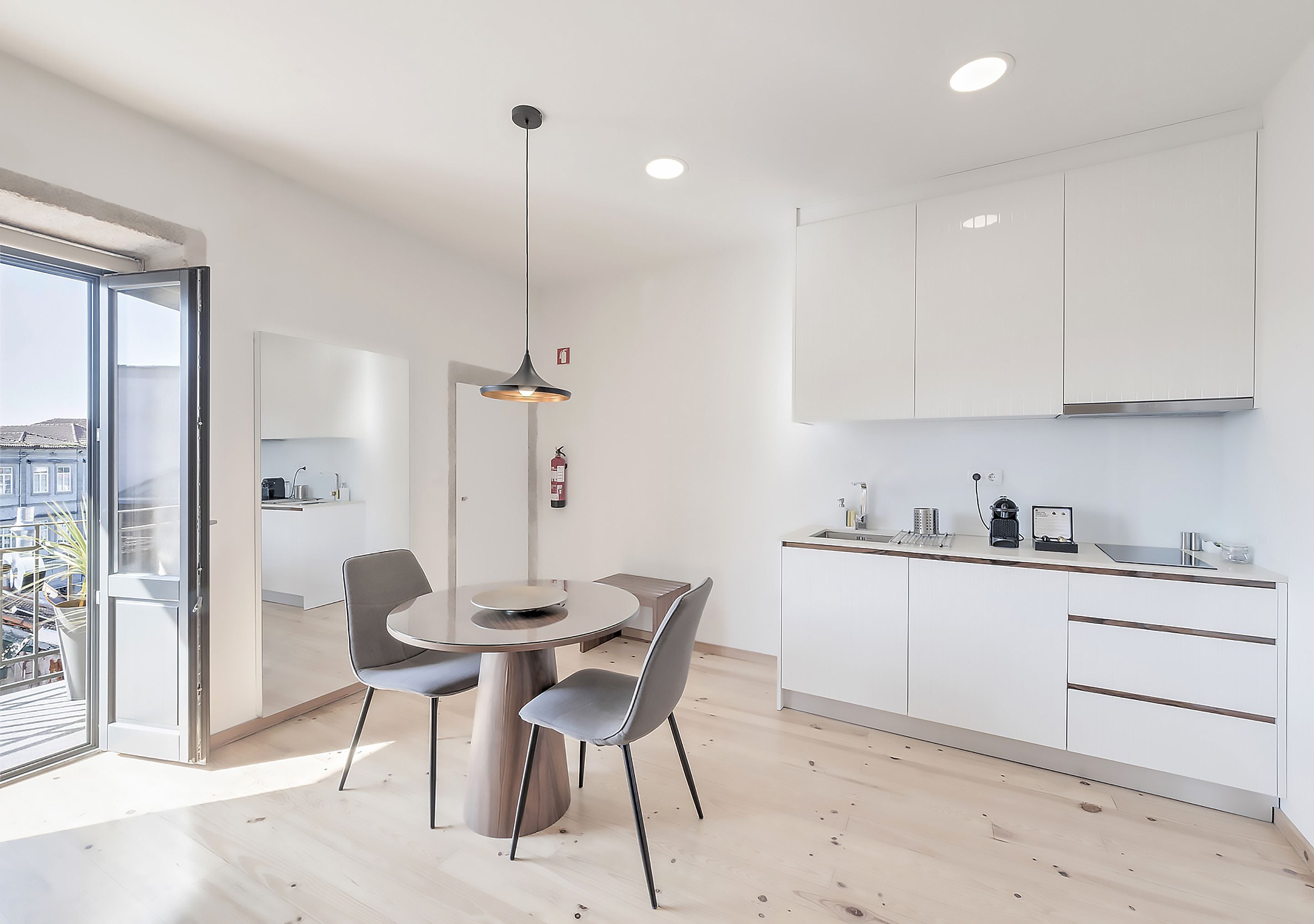 A modern kitchen with white cabinets, a dining area with a round table and chairs, and a pendant light.