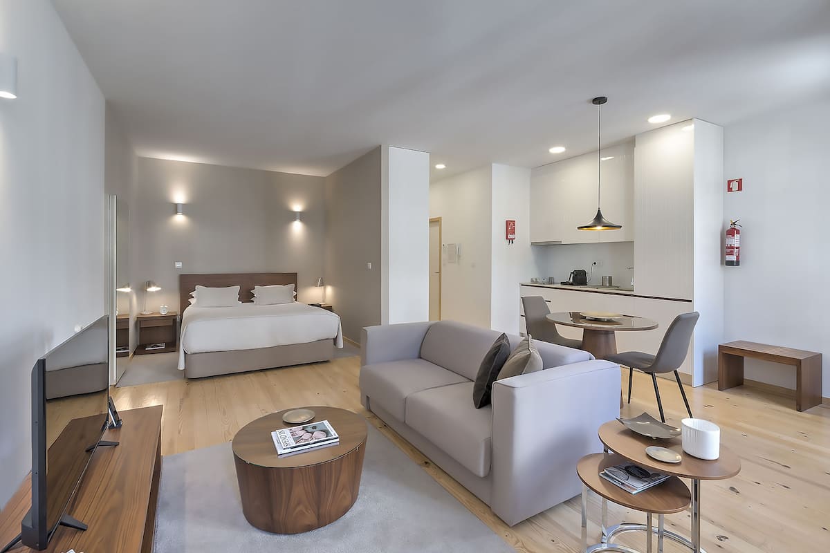 A modern hotel room with a bed, sofa, coffee table, and a small dining area.