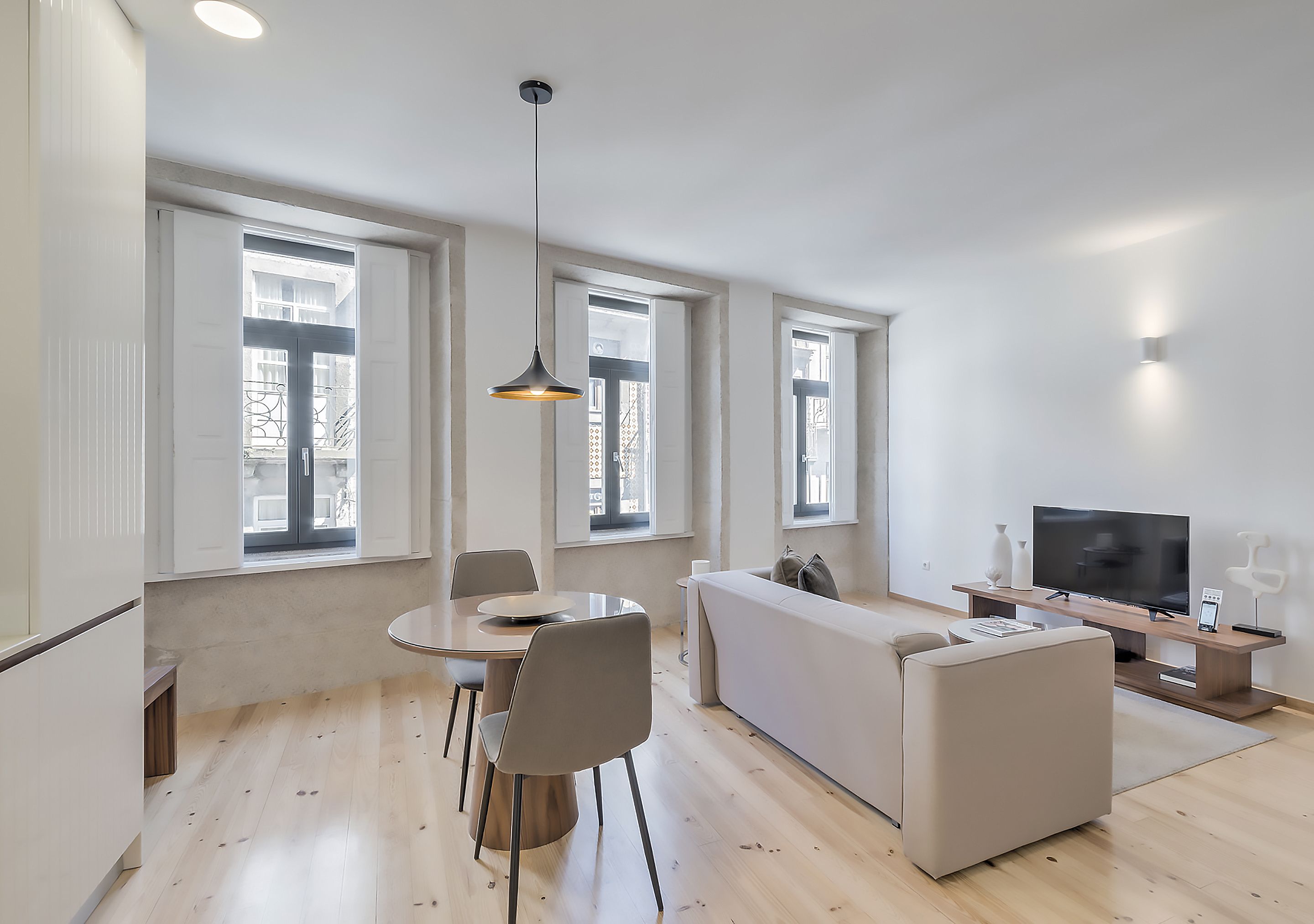 Una sala moderna con comedor, sofá, televisor y una lámpara colgante.