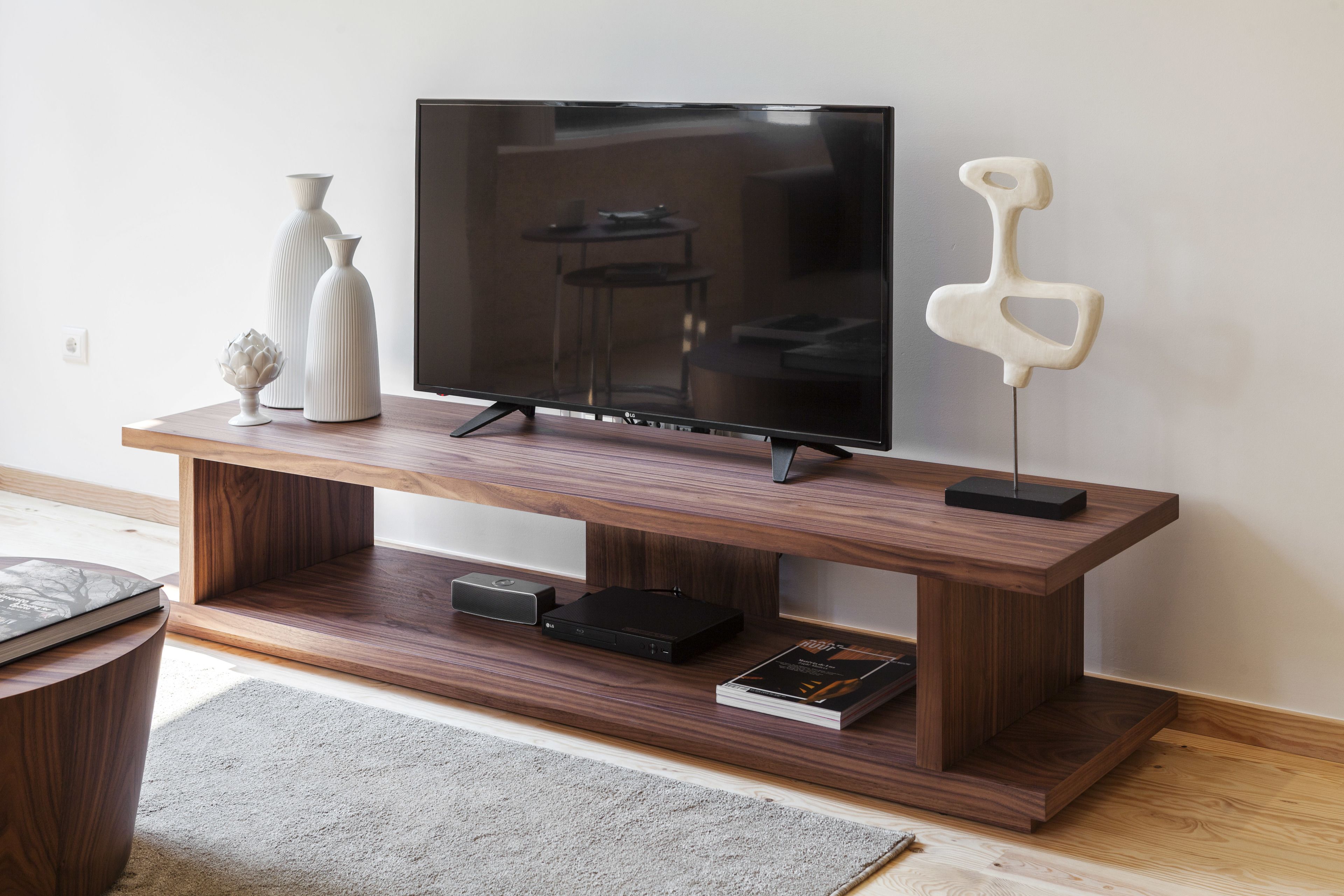 Un mueble bajo de madera con un televisor de pantalla plana, dos jarrones blancos, un objeto decorativo y un libro.