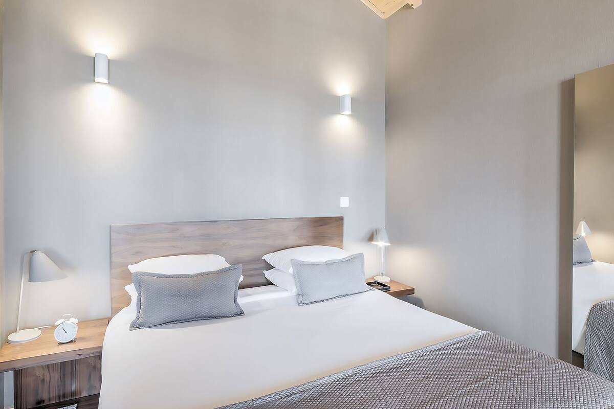 A hotel room with a bed, two bedside tables, a nightstand, a lamp, and a mirror.