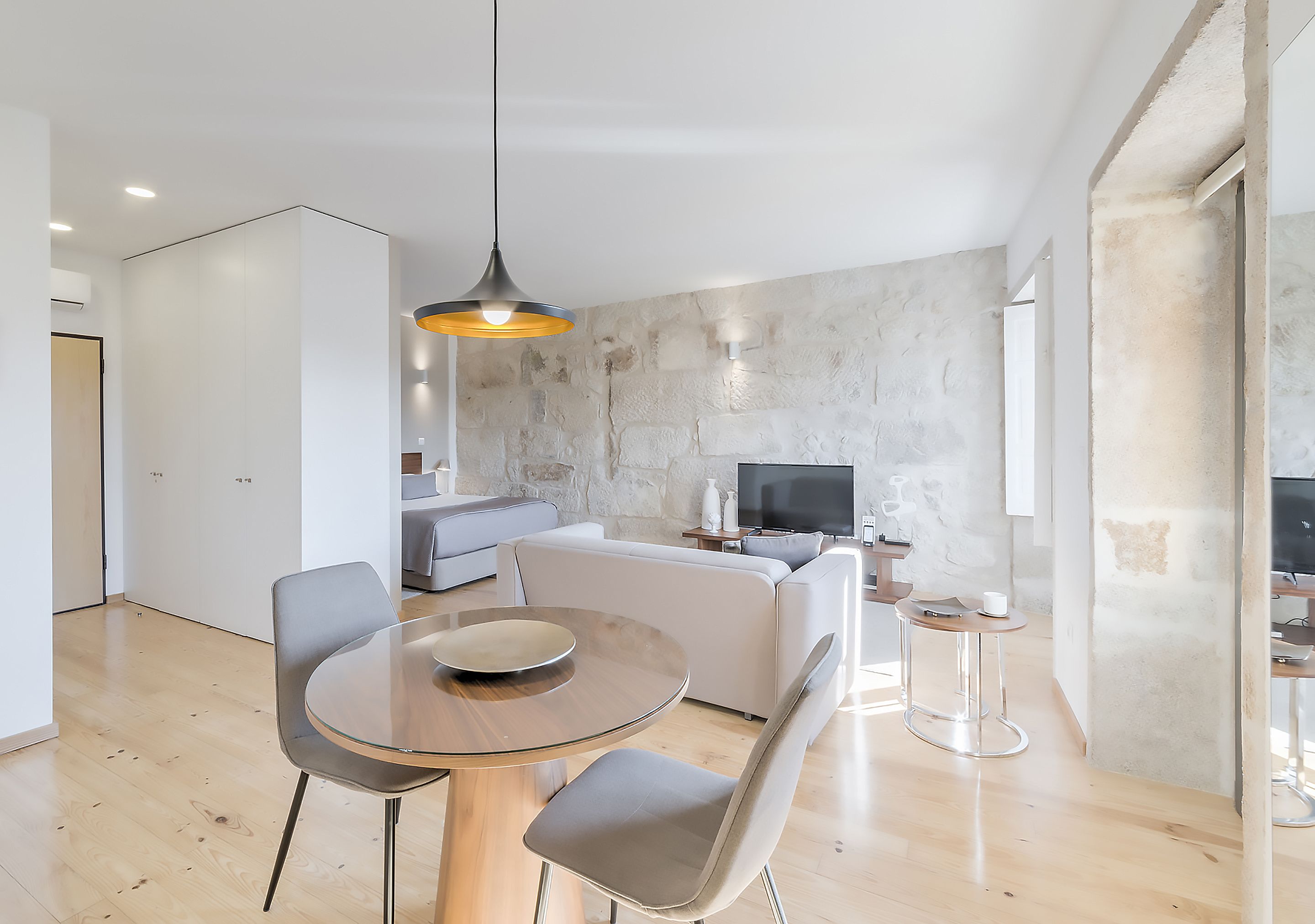 A modern living room with a dining area, a sofa, a TV, and a stone wall.
