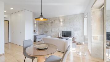 A modern living room with a dining area, a sofa, a TV, and a stone wall.
