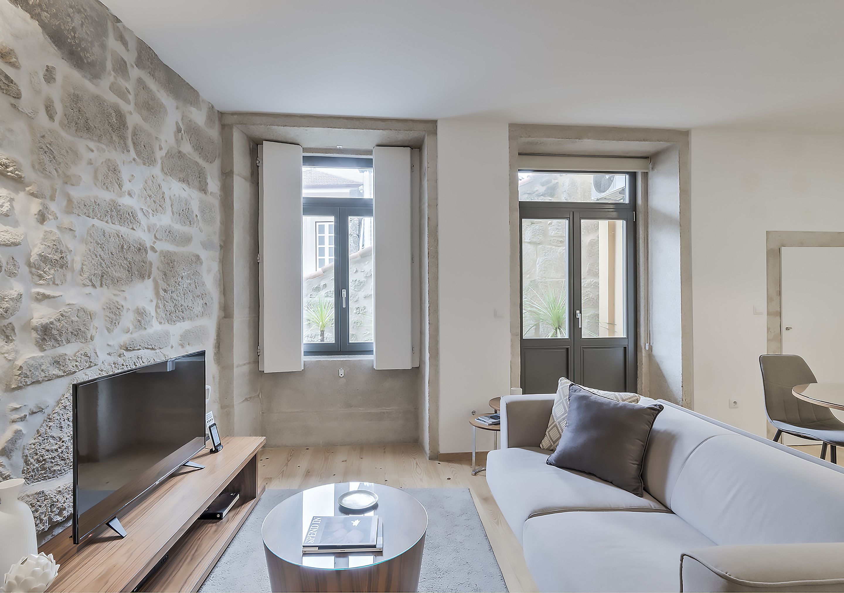 Un salón moderno con una pared de piedra, un televisor de pantalla plana, un sofá blanco y una mesa de centro.
