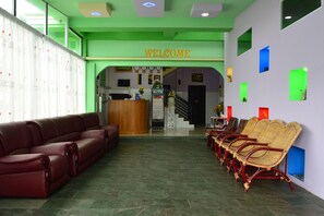 A reception area with a 'WELCOME' sign, a reception desk, a staircase, and a row of wicker chairs. - Hotel 99 (Pyin Oo Lwin)