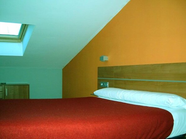 Una camera da letto con soffitto spiovente, una finestra a lucernario, una testiera in legno e una coperta letto rossa.