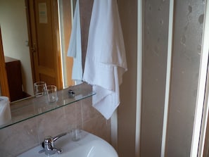 A bathroom with a glass shelf holding two glasses, a towel rack with a white towel, and a mirror reflecting the room. - Pardiola Baserria (Hernani)