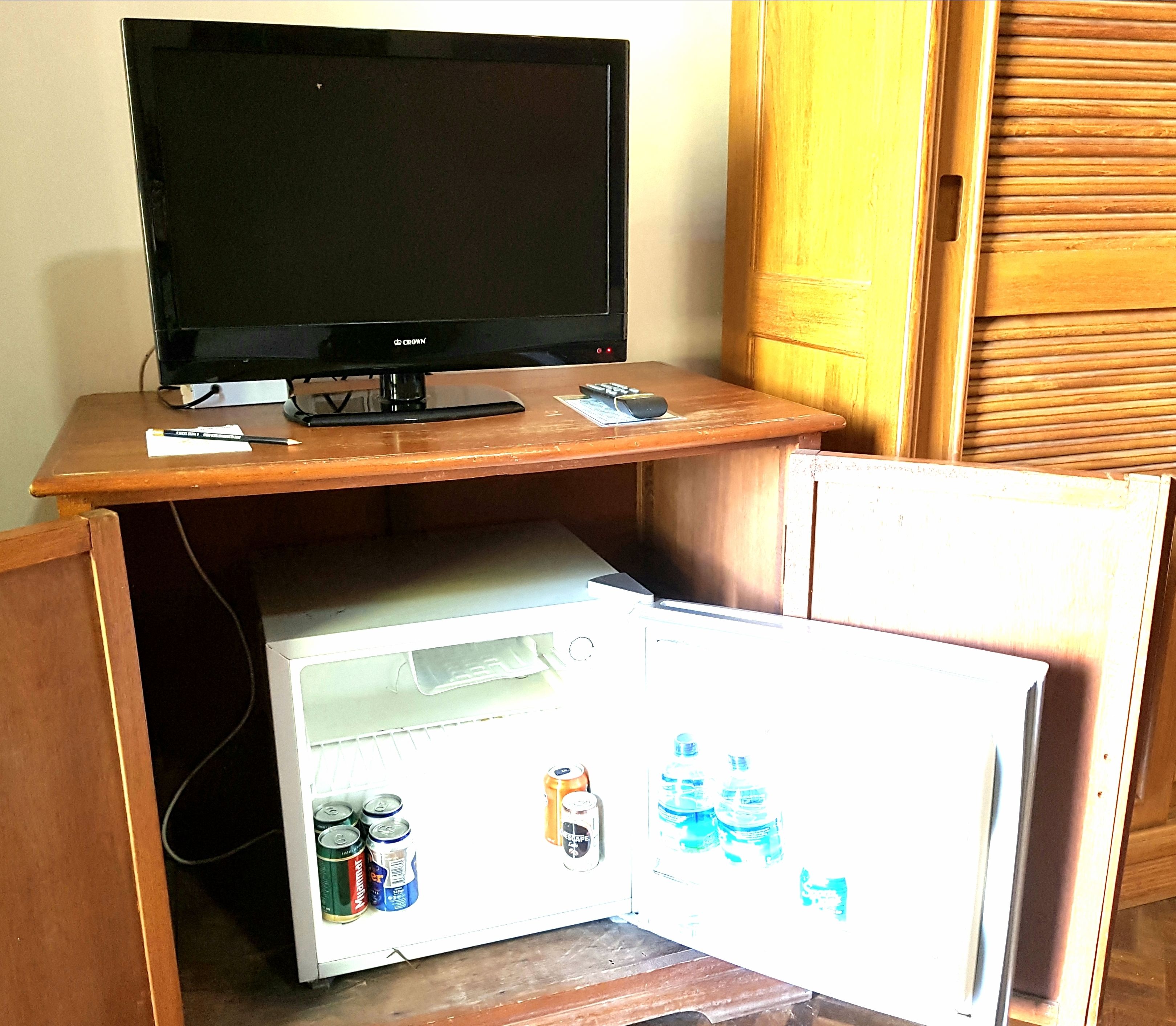 Een knus woongedeelte met een televisie op een houten standaard, een kleine koelkast met drankjes en een houten kast.