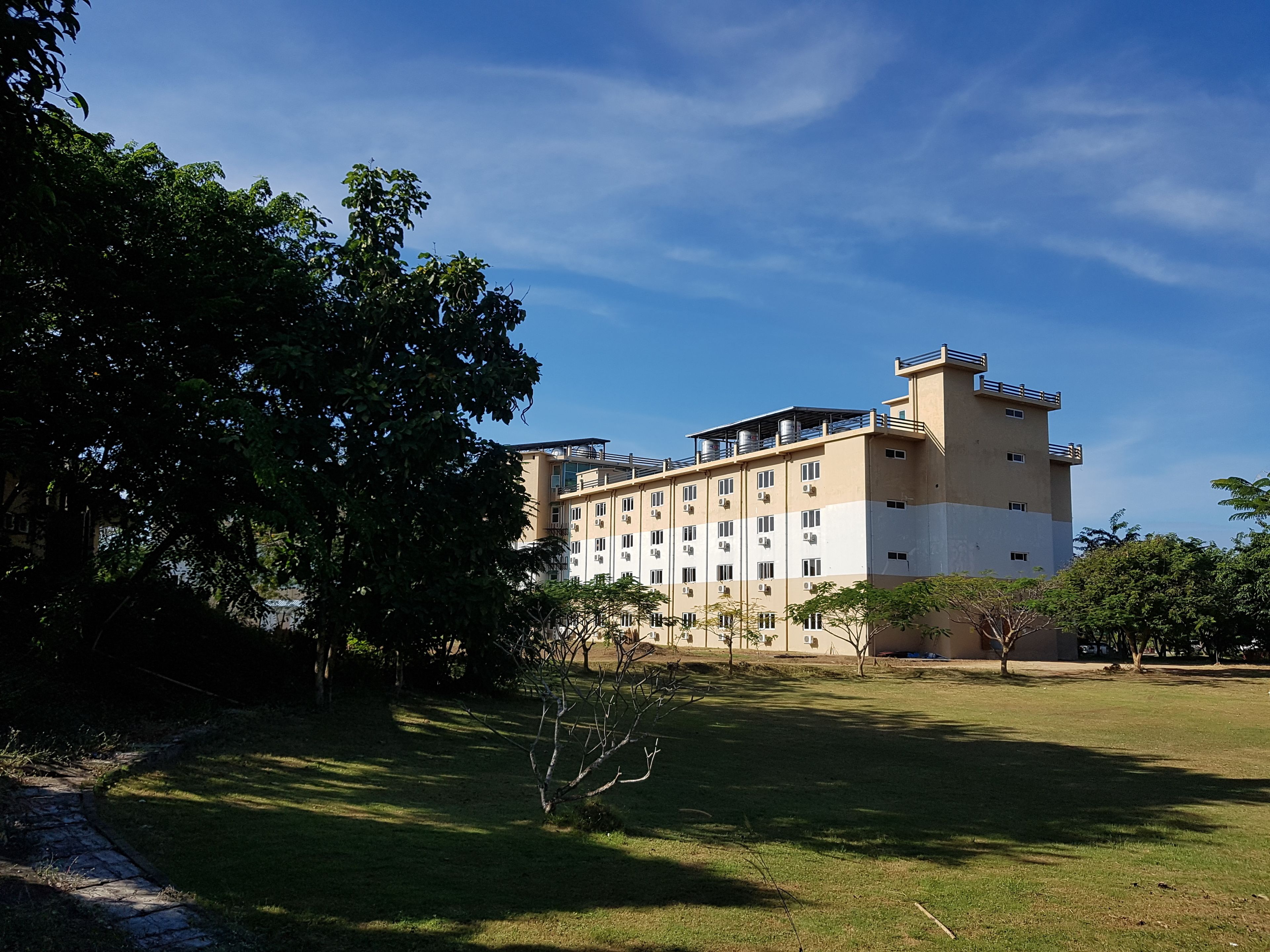 Un hôtel à plusieurs étages, doté d’un toit plat, entouré d’une zone herbeuse et d’arbres.