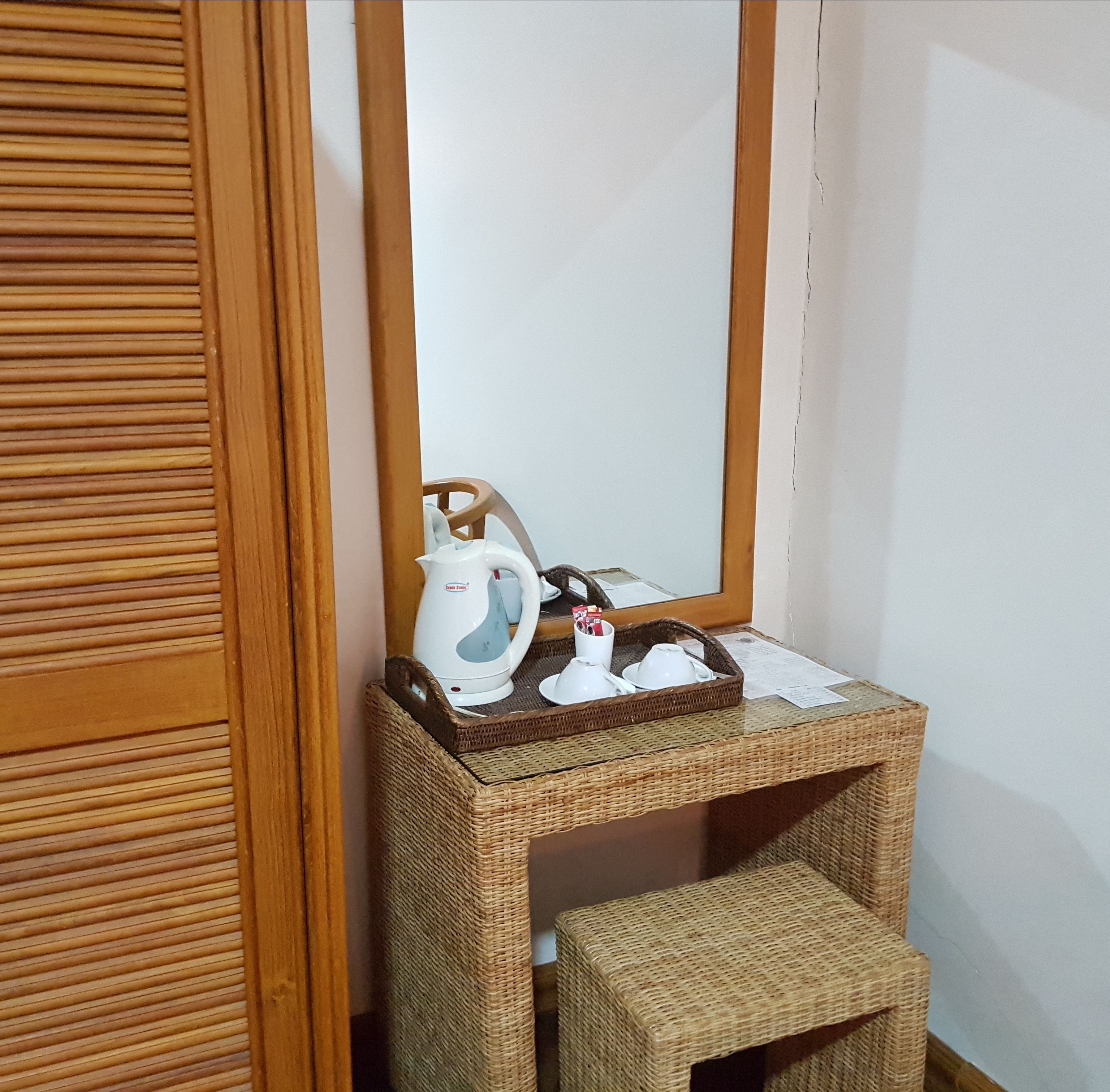 A small room with a wooden cabinet containing a kettle, cups, and a tray.