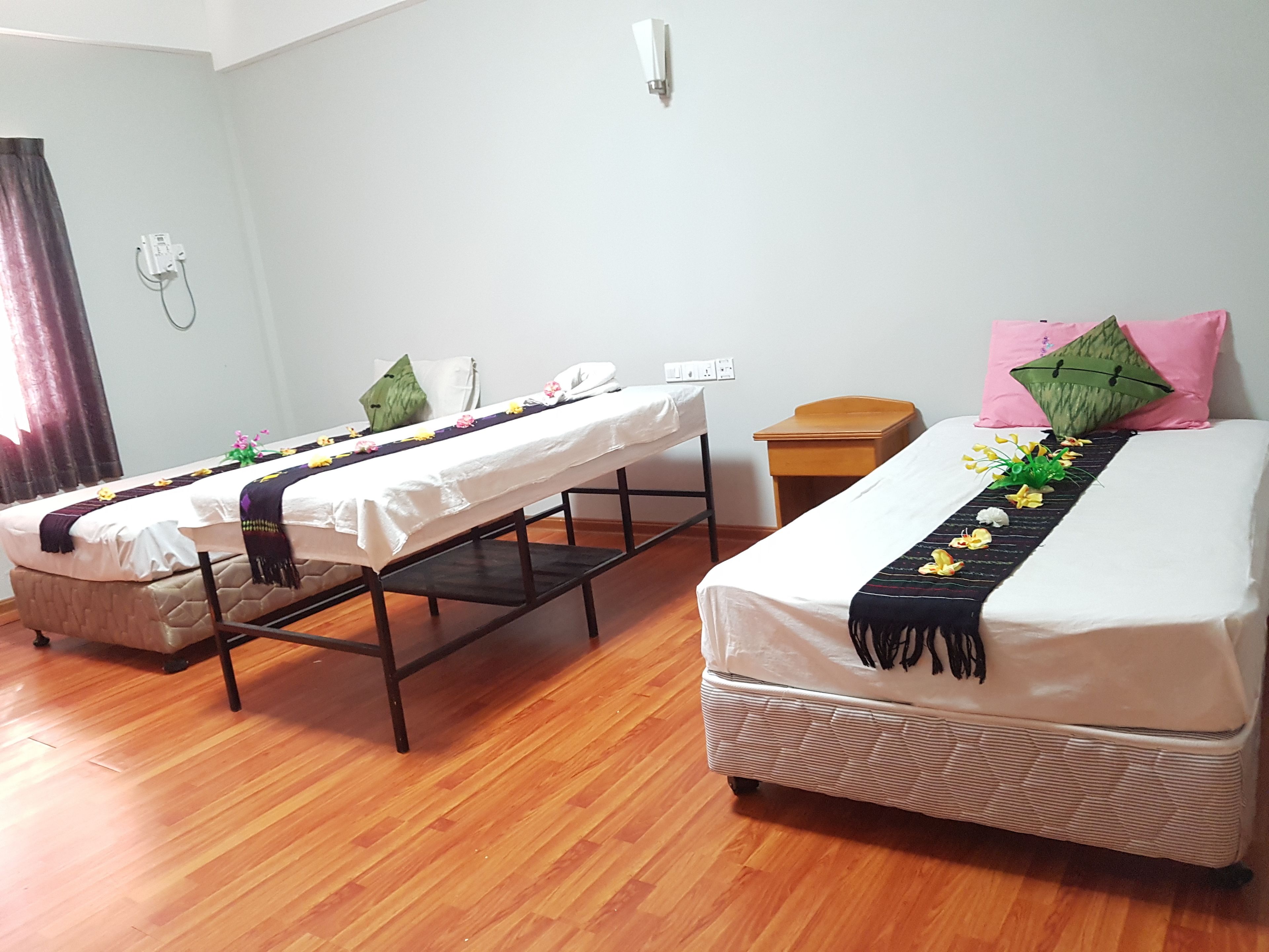 A room with two beds, a wooden floor, a small wooden table, and a wall socket.
