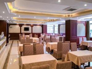 Un salón de conferencias de hotel con varias mesas y sillas, un televisor de pantalla plana y un ventanal grande.