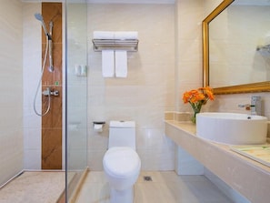 Un baño moderno con ducha envuelta en vidrio, inodoro y lavamanos con un florero.
