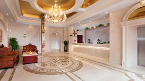 Una hall d'albergo con una reception, un lampadario, un divano in pelle e un pavimento decorato.