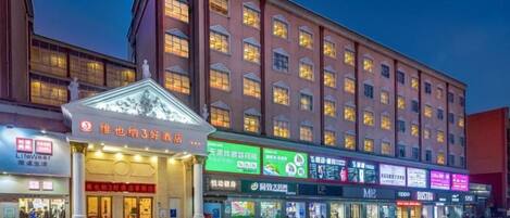 A hotel with multiple floors, a well-lit entrance, and various shops on the ground level.