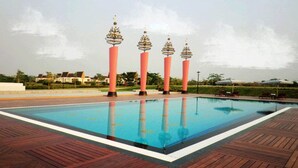 Una piscina con cubierta de madera y cuatro altos pilares rosados con detalles dorados.