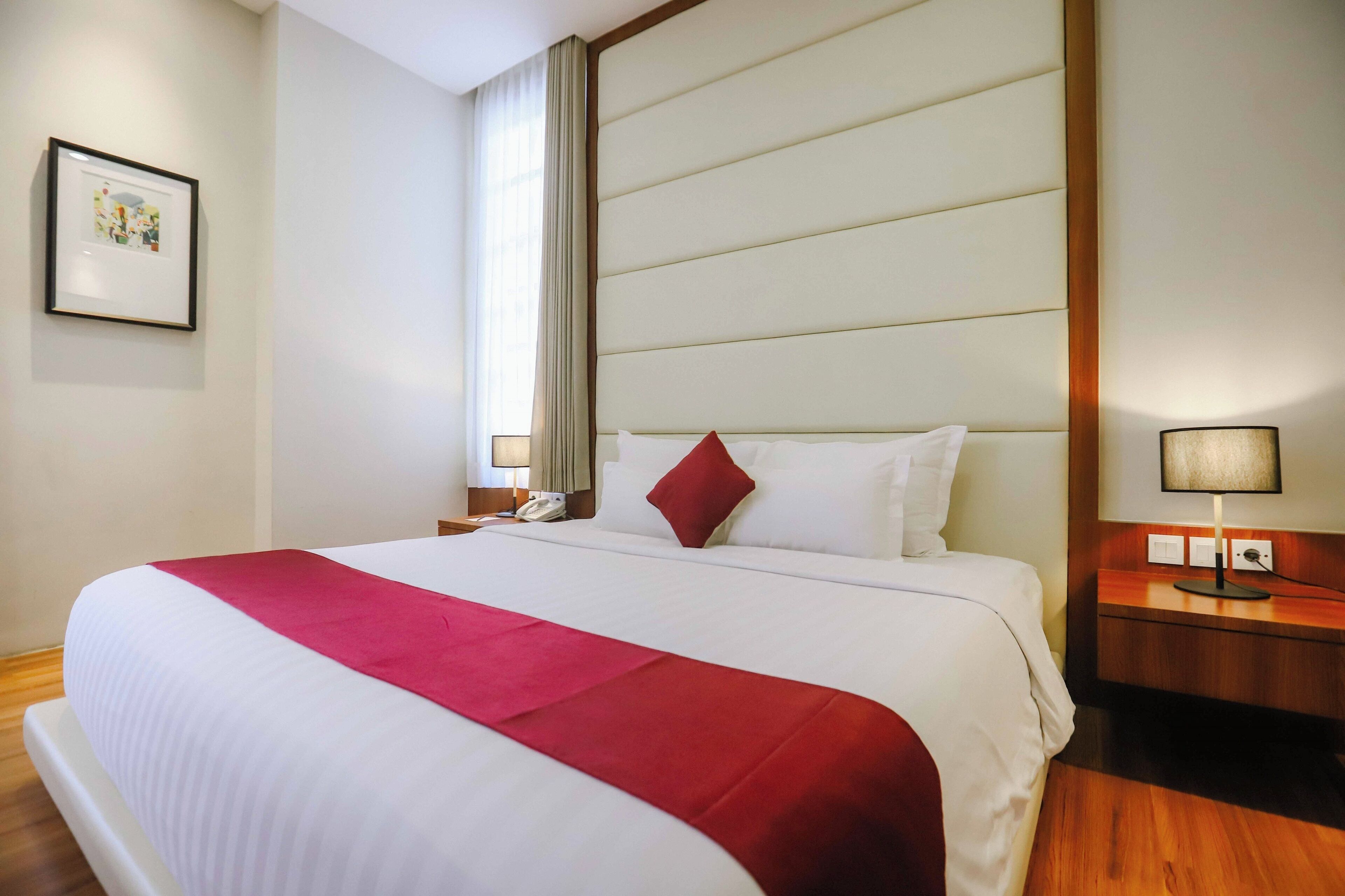 Quarto de hotel com uma cama grande, mesa de cabeceira, abajur e um quadro na parede.